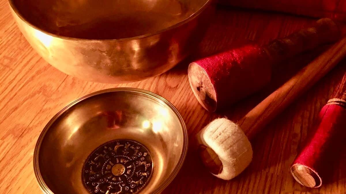 Close-up of Tibetan singing bowls and mallets on a wooden surface, lit by warm light – Primal Sound soundbath instruments for relaxation and wellbeing.