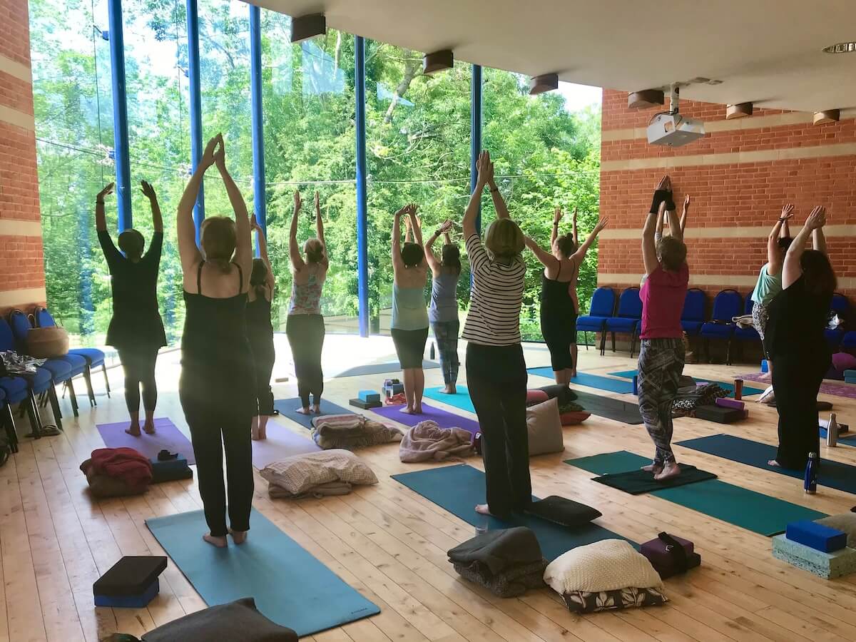Calm Within Active Session – Group Stretching in Natural Light Studio Group practising a gentle standing stretch in a bright, peaceful studio during a Calm Within active session.