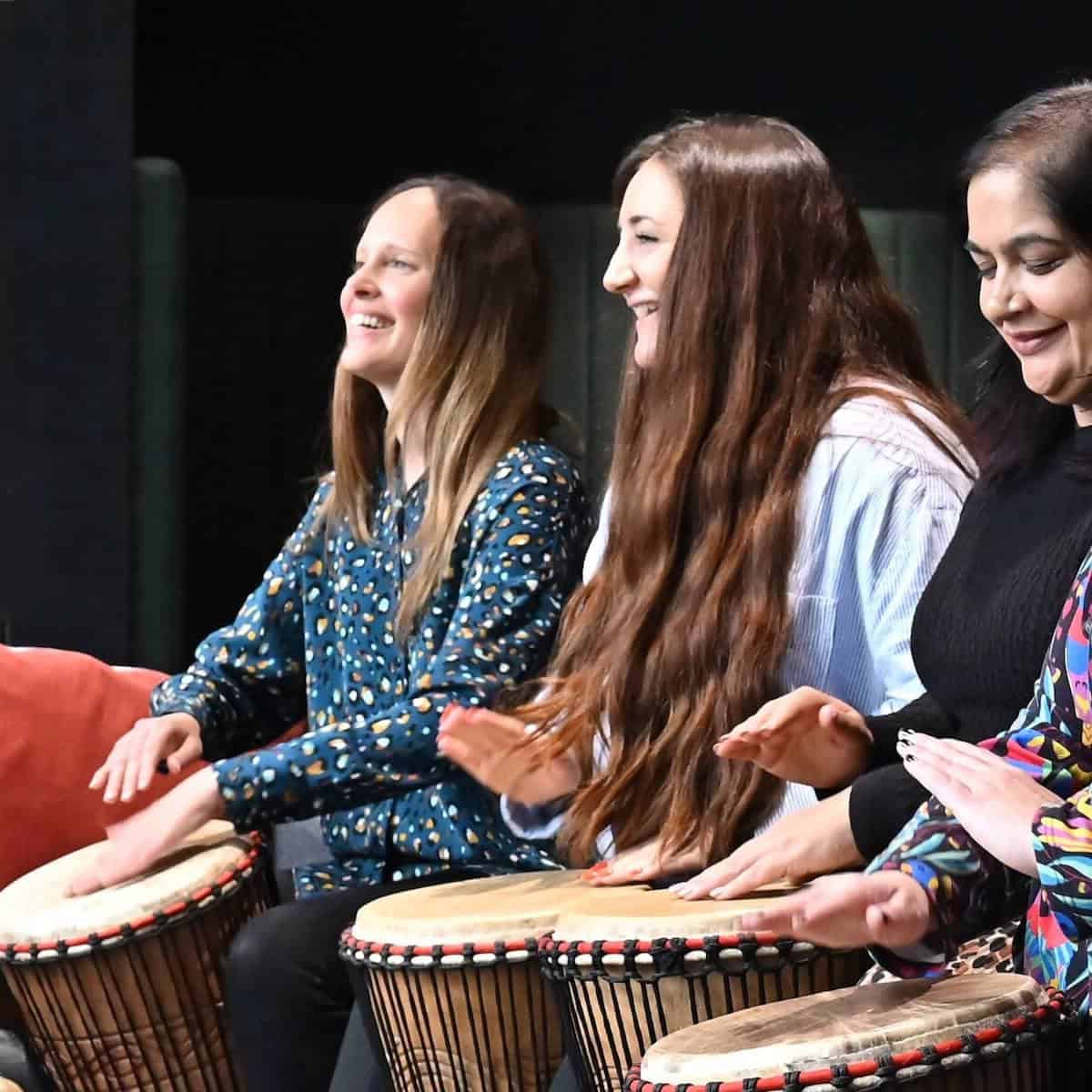 Colleagues smiling and drumming together in a corporate wellbeing session with Primal Sound.